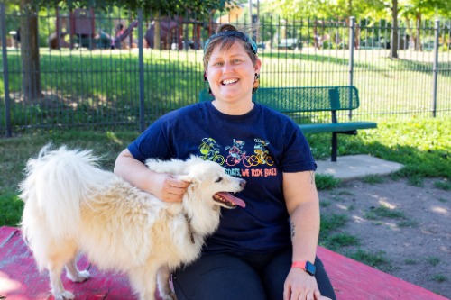 Image of woman with Cap backwards smiling and petting her dog while kneeling