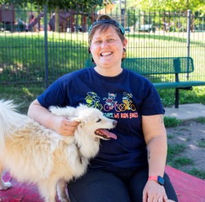 Image of woman with Cap backwards smiling and petting her dog while kneeling