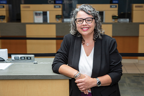 Image of lady in glasses smiling as she's leaning on a slccu station with transactions