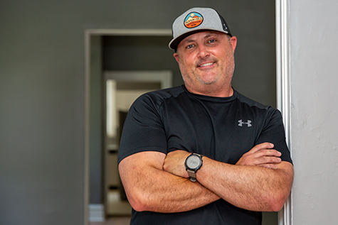 Image of man in black shirt with his arms crossed in a doorway smiling